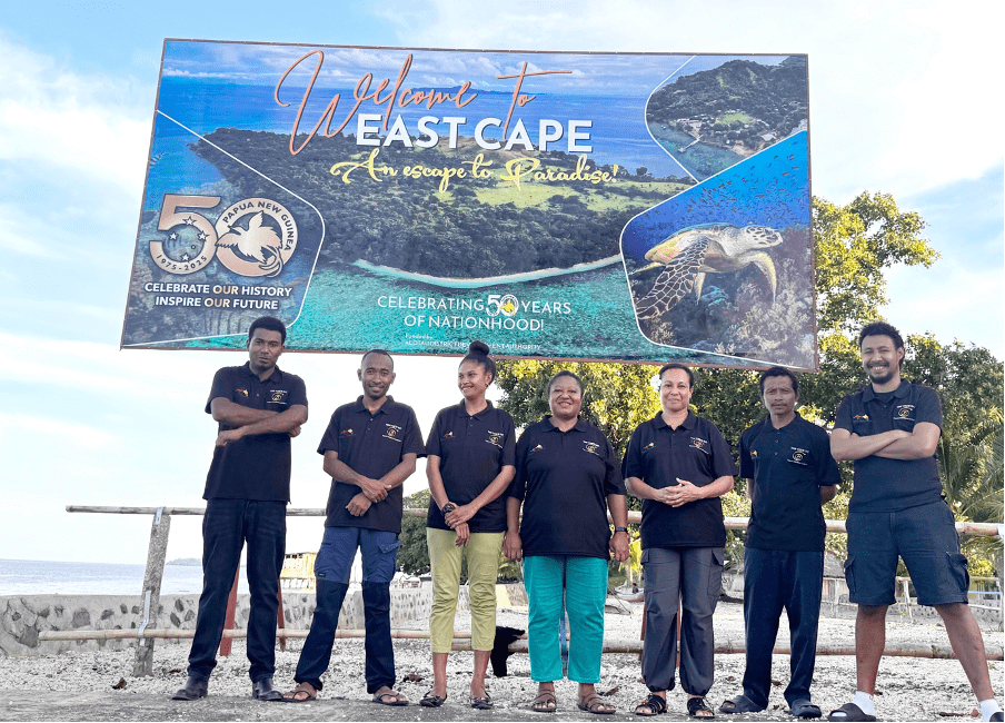 The Eastern Learners Team standing in front of a "Welcome to East Cape" sign at East Cape Point, Milne Bay Province, PNG.