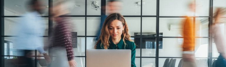 A woman working on a computer with blurred activity behind her