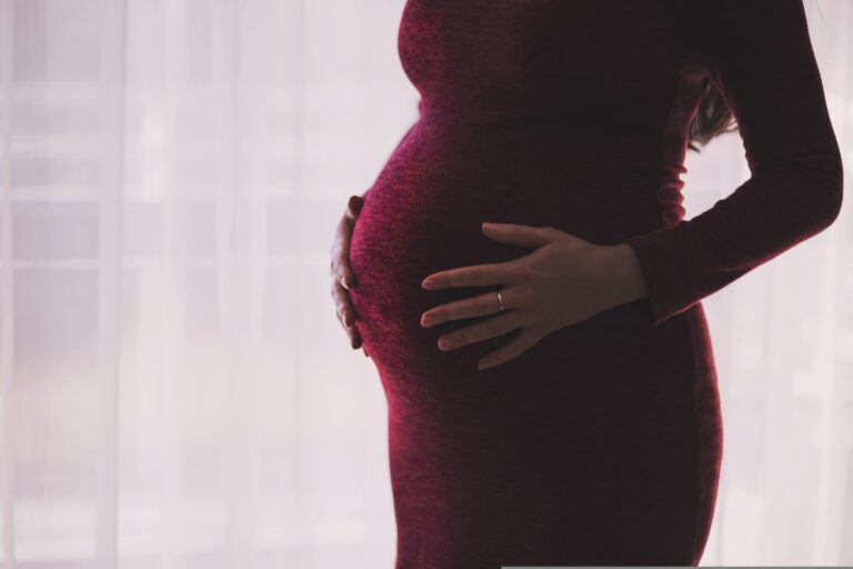 Pregnant woman holding stomach against a light background